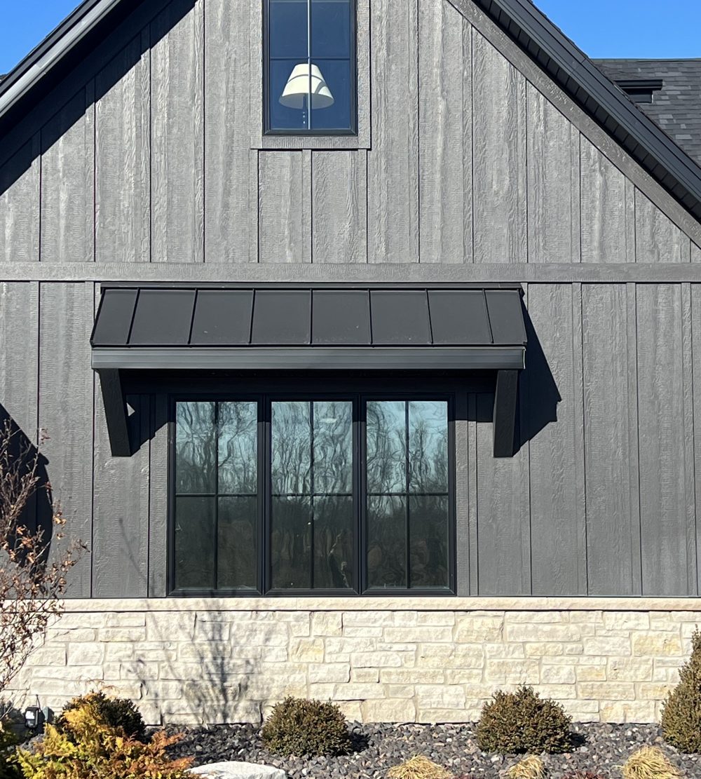 Grey board-and-batten home with black-frame windows fitted with window film